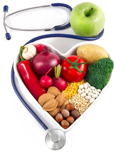 Stethoscope and apple lying next to a heart-shaped bowl full of healthy vegetables and legumes